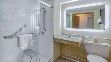 Une salle de bain avec une douche à parois de verre, des toilettes blanches, un lavabo avec un miroir au-dessus et un porte-serviettes.