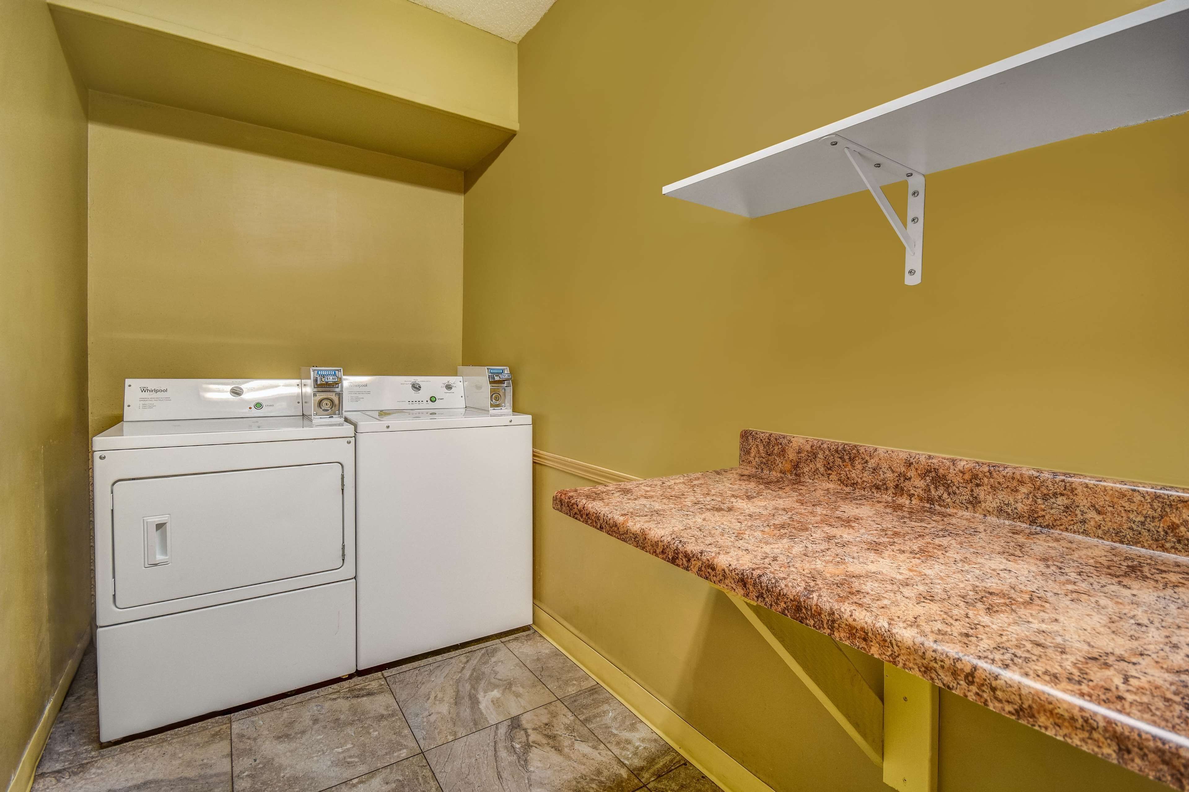 A laundry room with a washing machine and dryer, a granite countertop, and yellow walls.