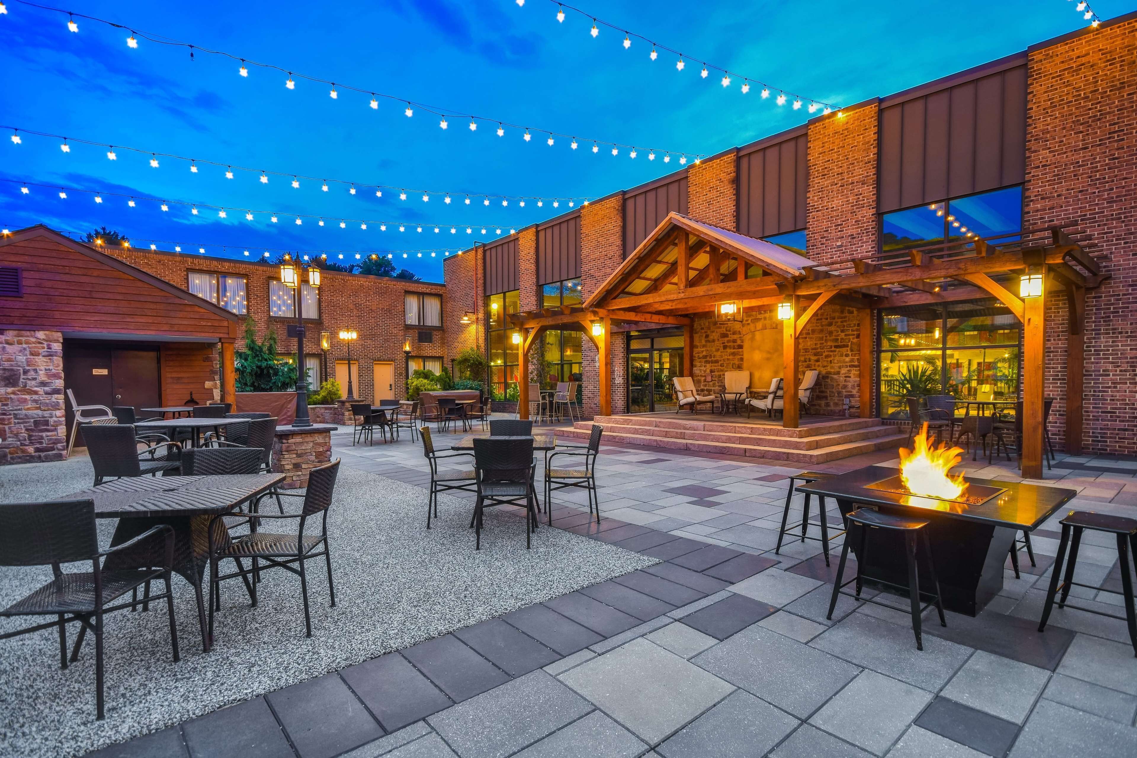 An outdoor patio area with tables and chairs, a fire feature, and string lights.