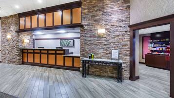 Zona de recepción con pared de piedra, mostrador de madera y un letrero que indica una cafetería.