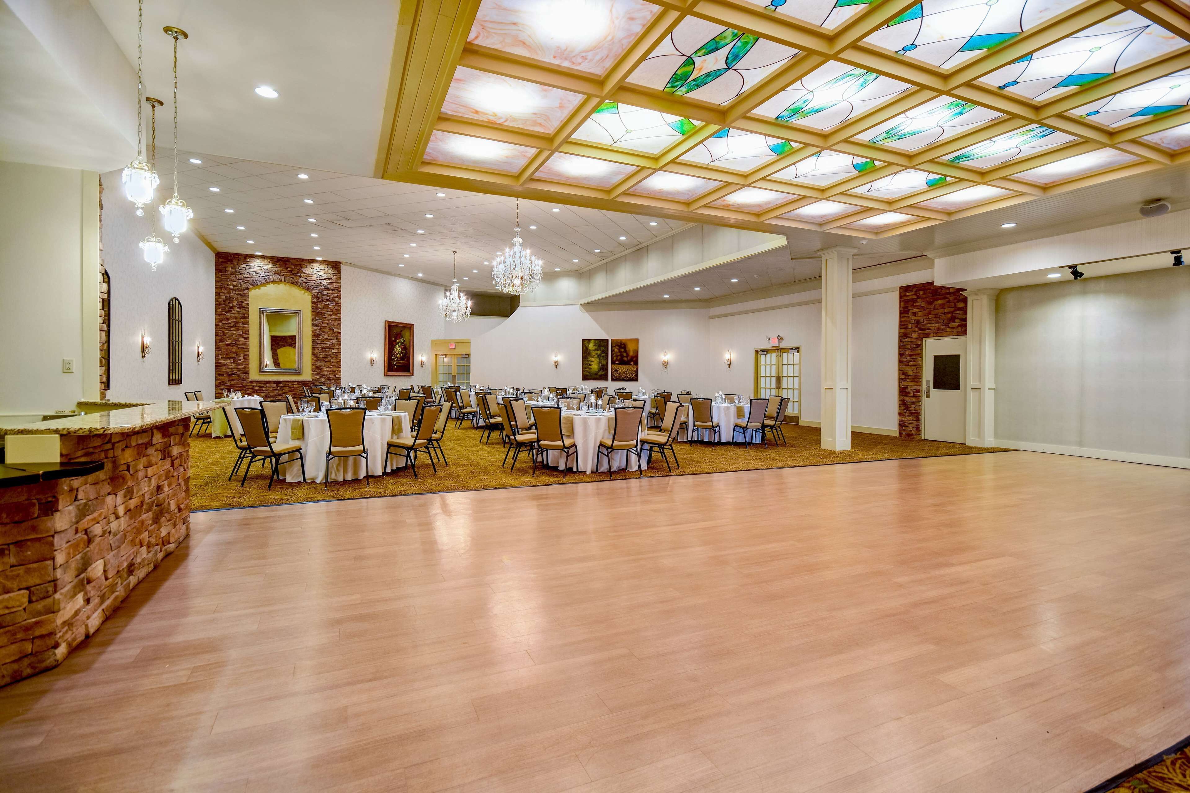 Une vaste salle de banquet dotée de hauts plafonds, d’un lustre central et d’un plafond en vitrail. Des tables sont disposées pour les repas, et les murs sont agrémentés d’éléments en briques.