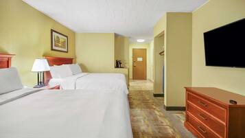 Quarto de hotel com uma cama grande, uma mesa com luminária, cômoda, televisão e um quadro na parede.