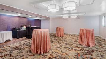 Un salón de conferencias con alfombra estampada, una zona de bar con botellas y tres mesas redondas cubiertas con telas.