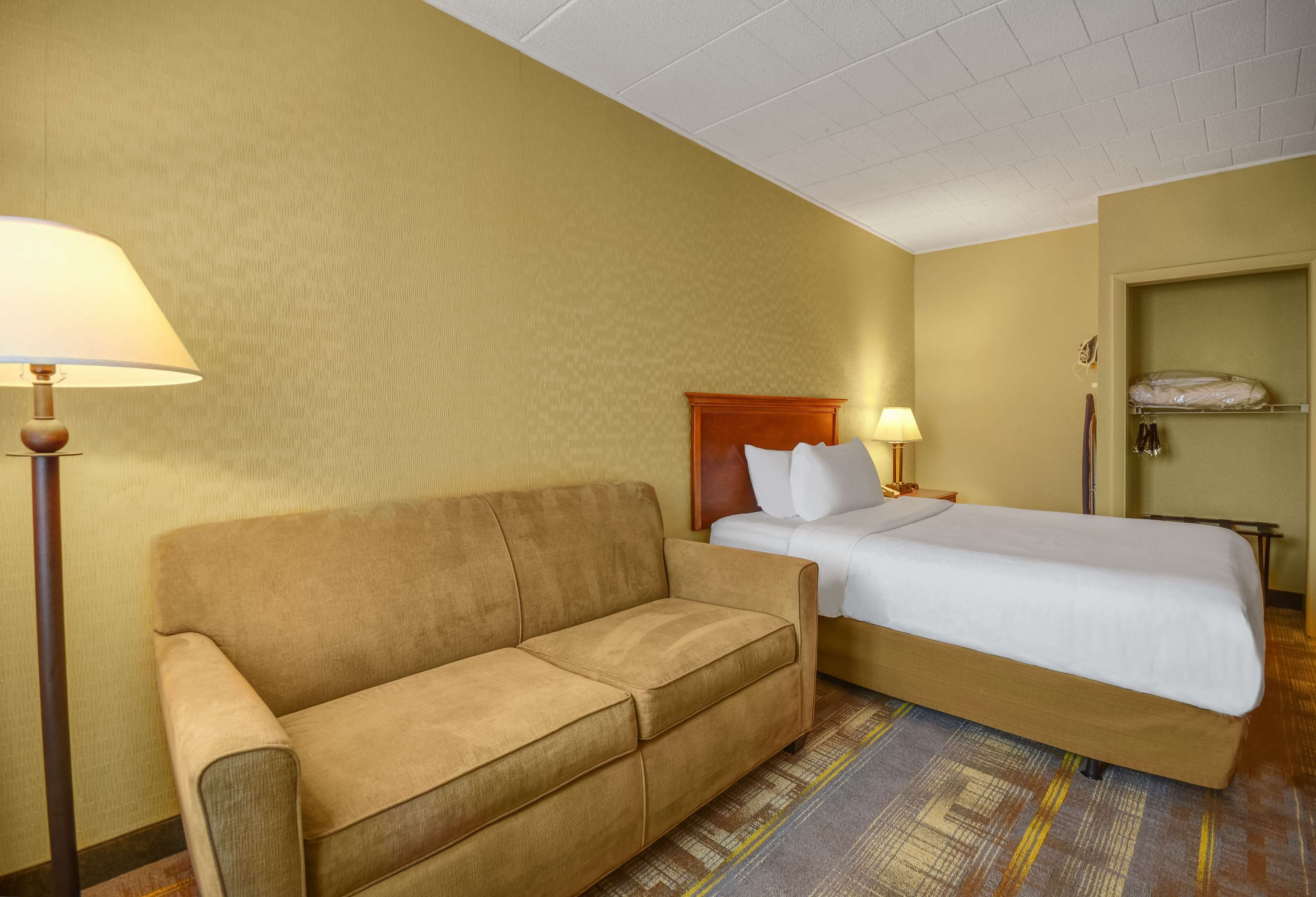 A hotel room with a bed, a sofa, a lamp, and a wardrobe.