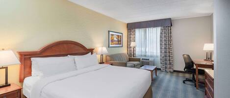 A hotel room with a large bed, a desk, a chair, a sofa, and a window with curtains.