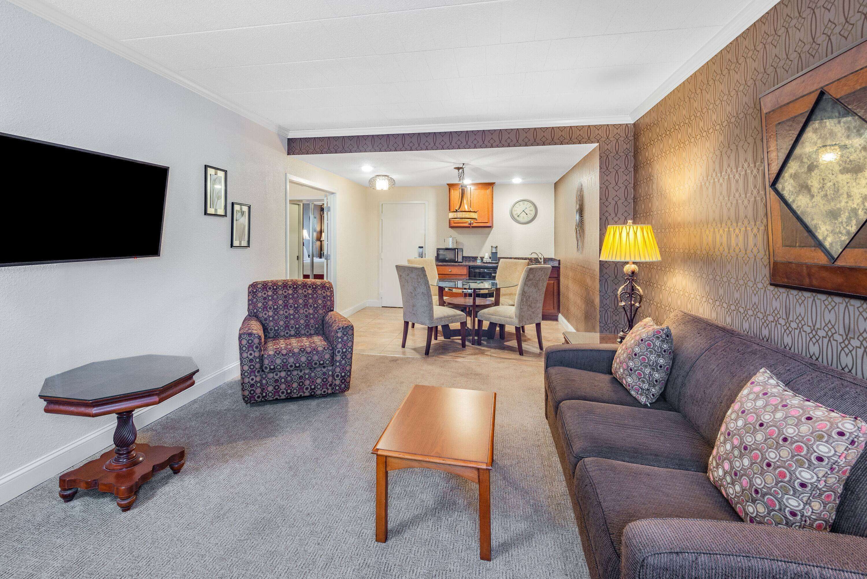 A living room with a sofa, armchair, coffee table, TV, and dining area with chairs and a table.