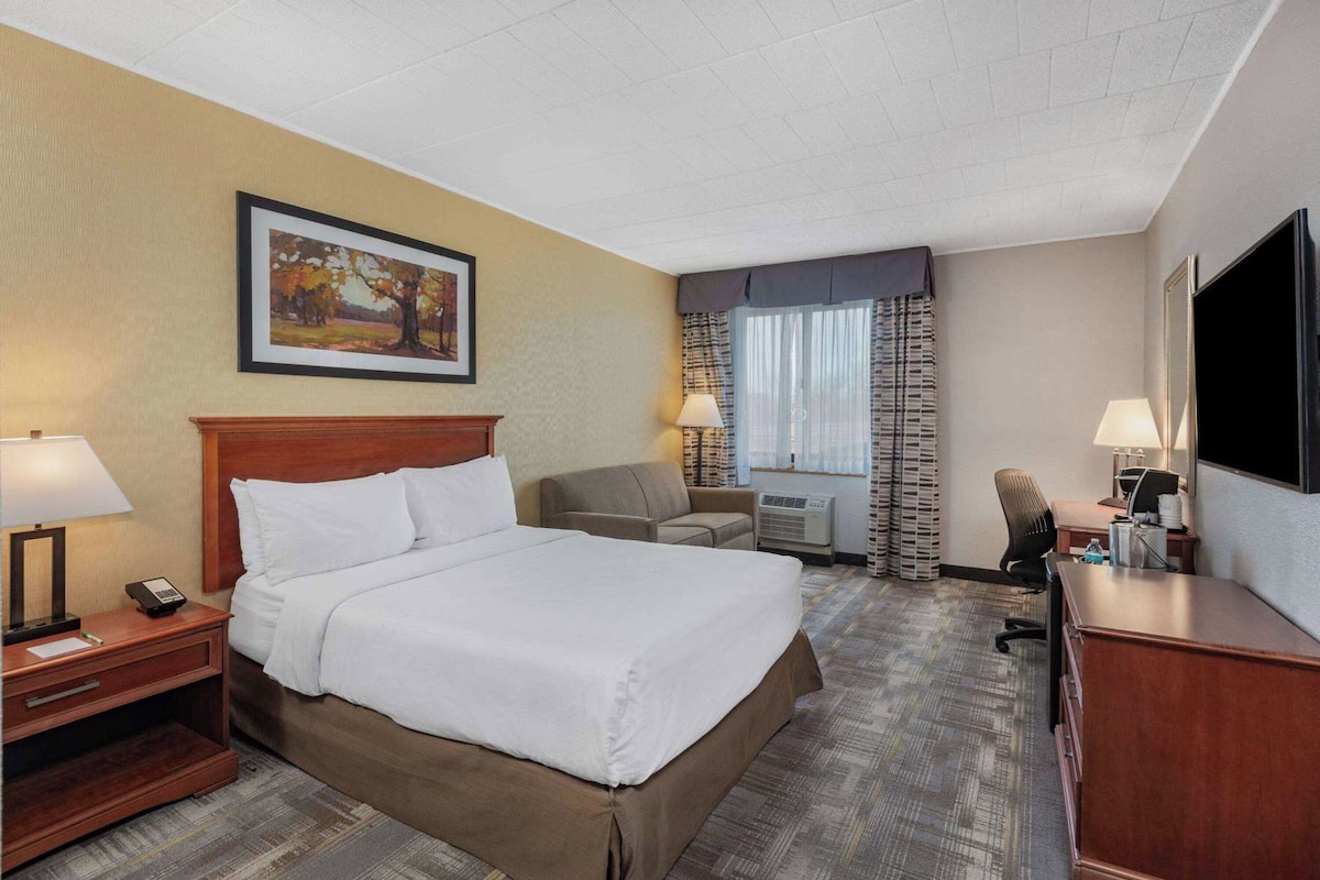 A hotel room with a bed, a desk, a chair, a TV, and a window with curtains.
