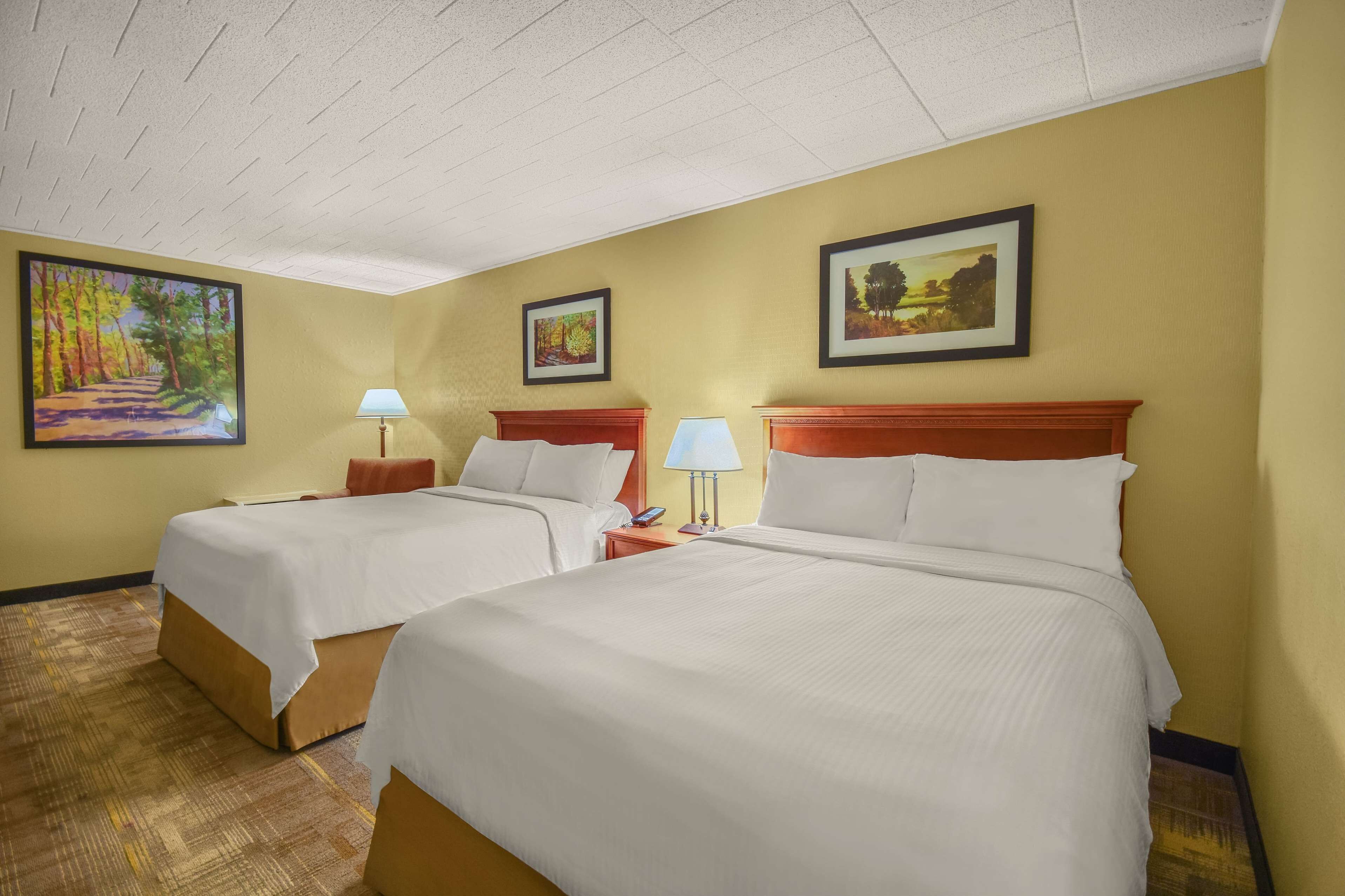 A hotel room with two beds, a large painting on the left wall, and a smaller painting above the right bed.