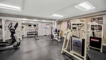 Ein Fitnessstudio mit unterschiedlichen Trainingsgeräten, darunter ein Laufband, Kraftgeräte und ein Ventilator.