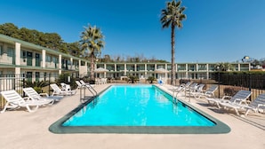 A swimming pool with lounge chairs and palm trees, surrounded by a hotel building.