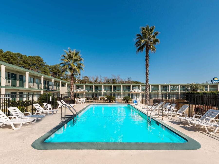 Ein Swimmingpool mit Liegestühlen und Palmen, umgeben von einem Hotelgebäude.