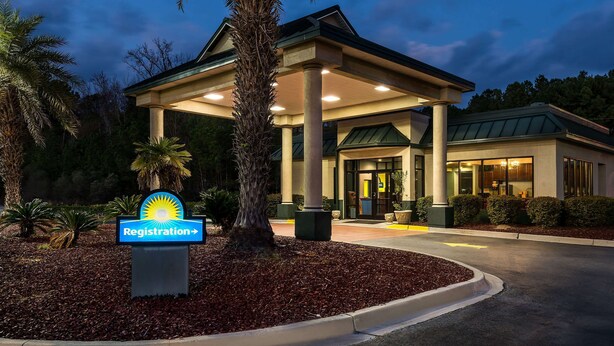 A hotel with a registration sign, a covered entrance, and a well-maintained outdoor area with trees and shrubs.