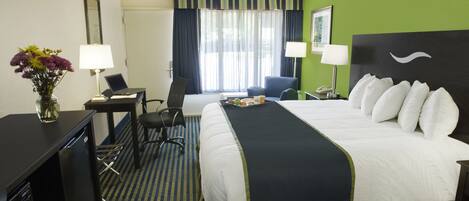 A hotel room with a bed, desk, chair, and a desk lamp.