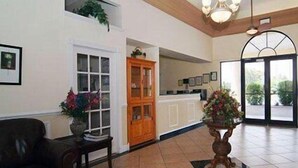 A lobby with a dark leather sofa, a wooden table with a vase, a wooden cabinet, and a tiled floor. - Quality Inn & Suites Mt Dora North (Mount Dora)