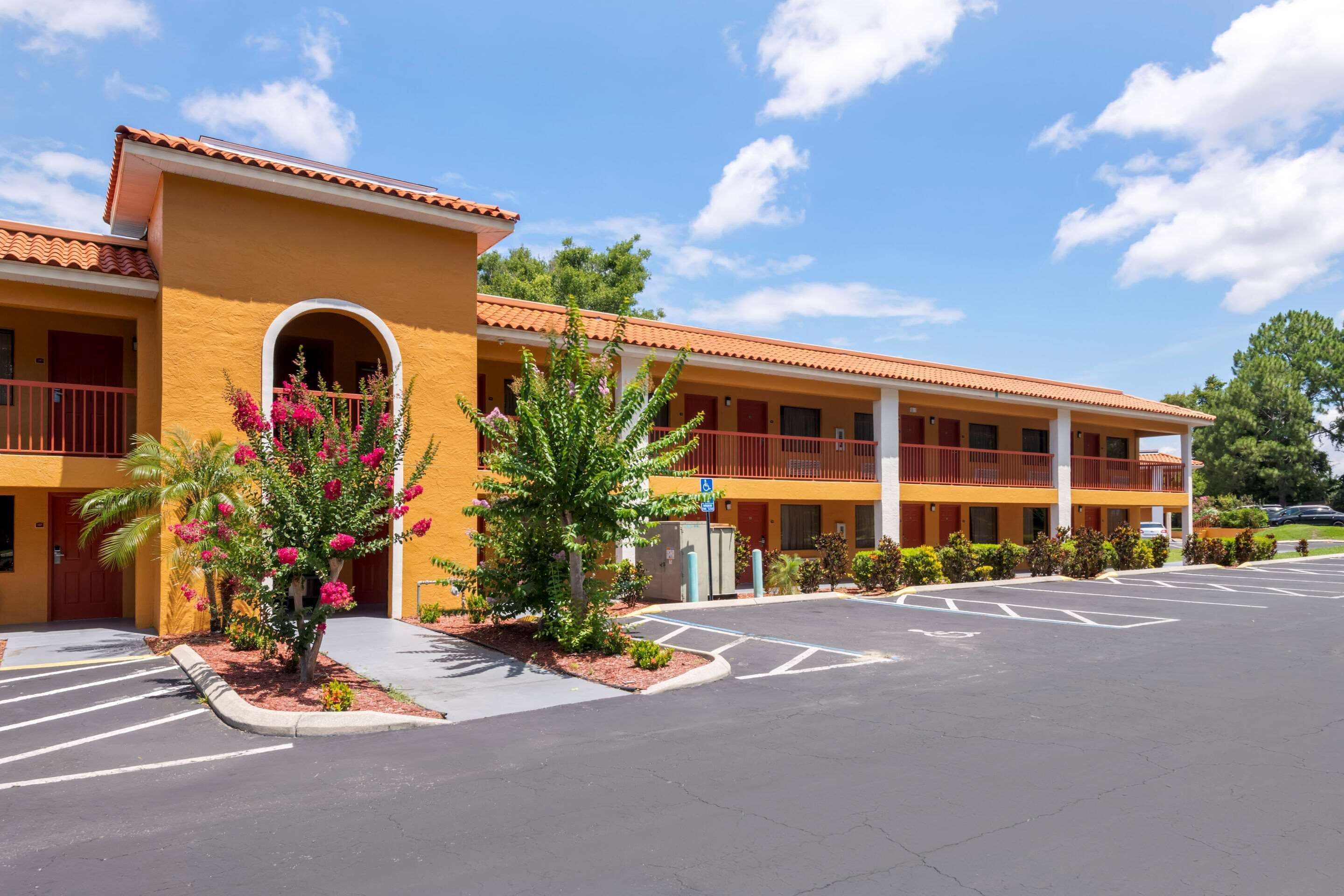 A hotel with a yellow facade, multiple balconies, and a parking lot with marked spaces.