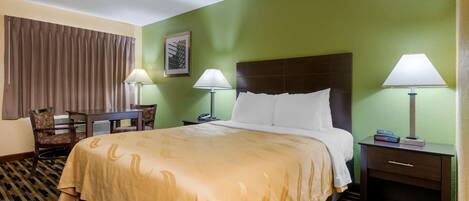 A hotel room with a bed, two bedside tables with lamps, a chair, a desk, and a patterned carpet.