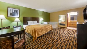 A hotel room with a bed, two bedside lamps, a desk with a chair, a television, and a bathroom visible through an open door. - Quality Inn & Suites Mt Dora North (Mount Dora)