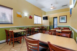 A dining area with multiple tables and chairs, a ceiling fan, and a television on the wall.
