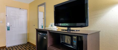 A hotel room with a flat-screen TV mounted on a wooden cabinet, a microwave, and a dishwasher.