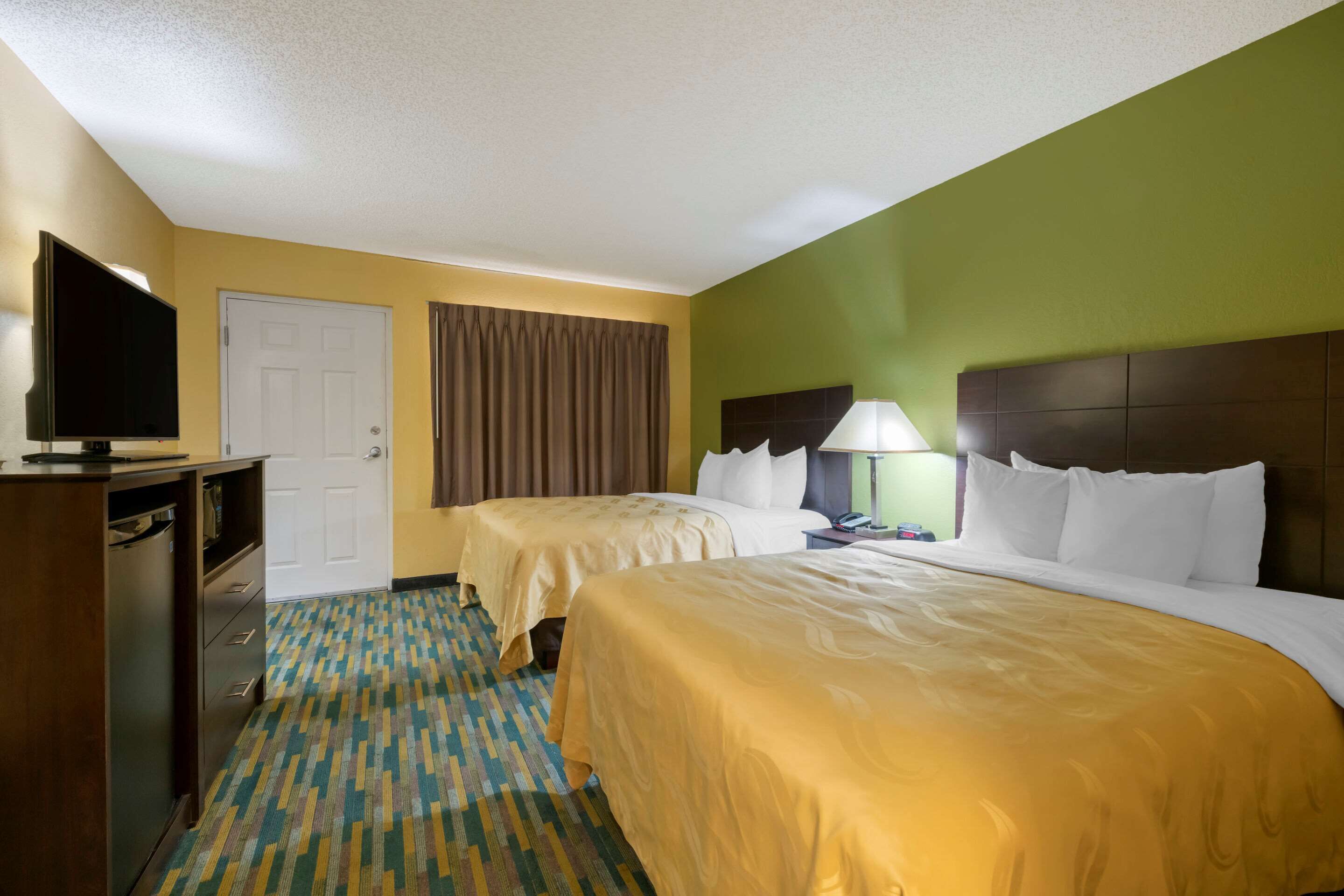 A hotel room with two beds, a television, a desk, and a patterned carpet.