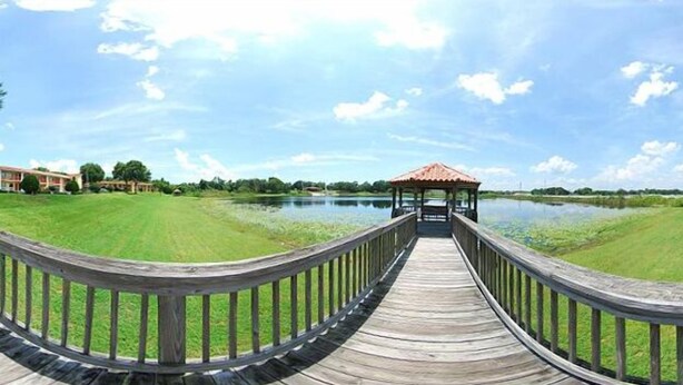 A wooden boardwalk leading to a gazebo over a body of water, surrounded by grassy areas and a building in the background. - Quality Inn & Suites Mt Dora North (Mount Dora)