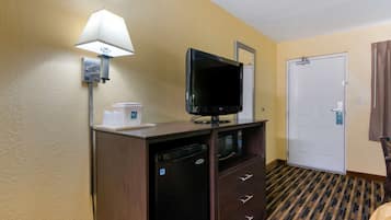 A hotel room with a flat-screen TV, a coffee maker, a microwave, a mini-fridge, a door, and a patterned carpet.