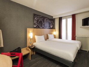 Habitación de hotel con dos camas, un escritorio, una silla, un televisor y una ventana con cortinas.