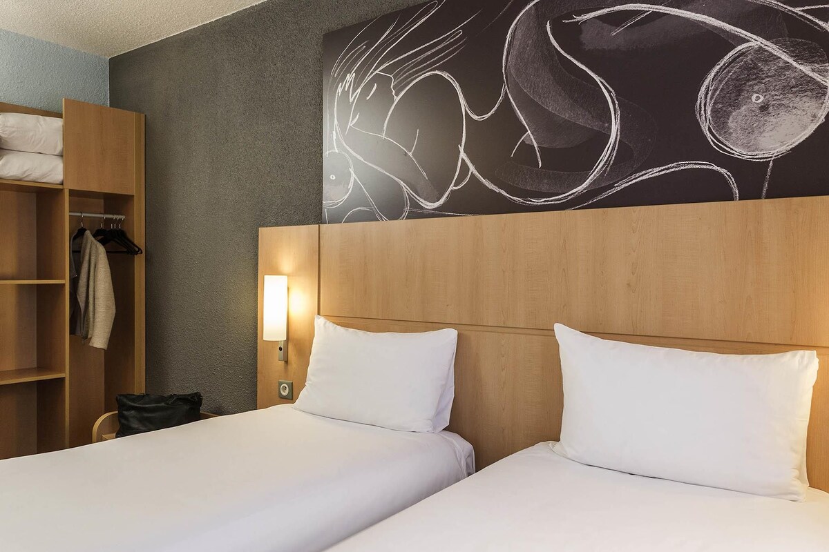 Ein Hotelzimmer mit zwei Betten, einem Kleiderschrank und einer Wandleuchte.