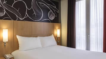 A hotel room with a large bed, two bedside lamps, a telephone, and a wall with abstract art.