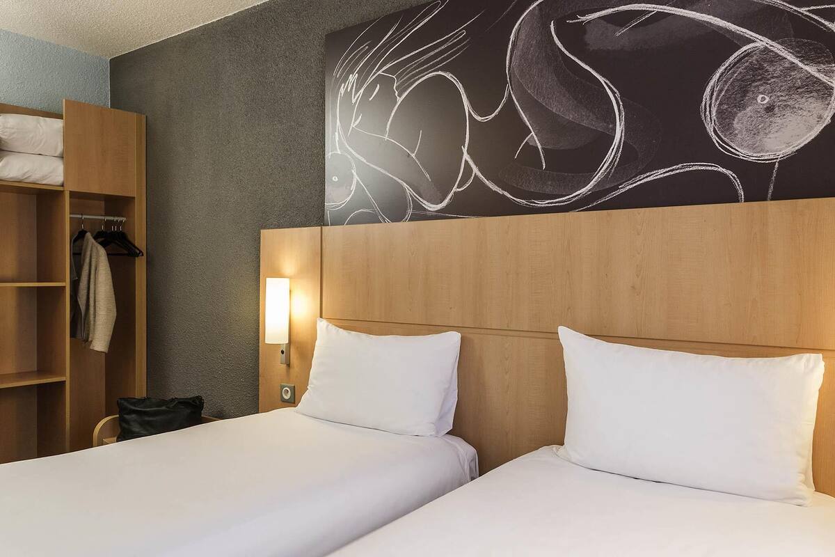 Una habitación de hotel con dos camas, un armario y una lámpara fijada a la pared.
