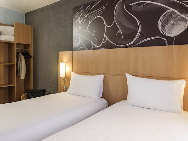 A hotel room with two beds, a wardrobe, and a wall-mounted light fixture.