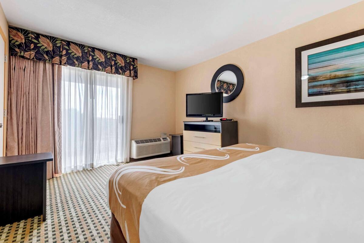 Una habitación de hotel con una cama grande, televisión, escritorio y un espejo en la pared.