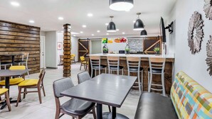 A modern dining area with wooden paneling, black pendant lights, and a central bar area with stools.