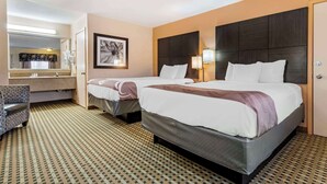 A hotel room with two beds, a large mirror, a framed artwork, a desk, and a patterned carpet.
