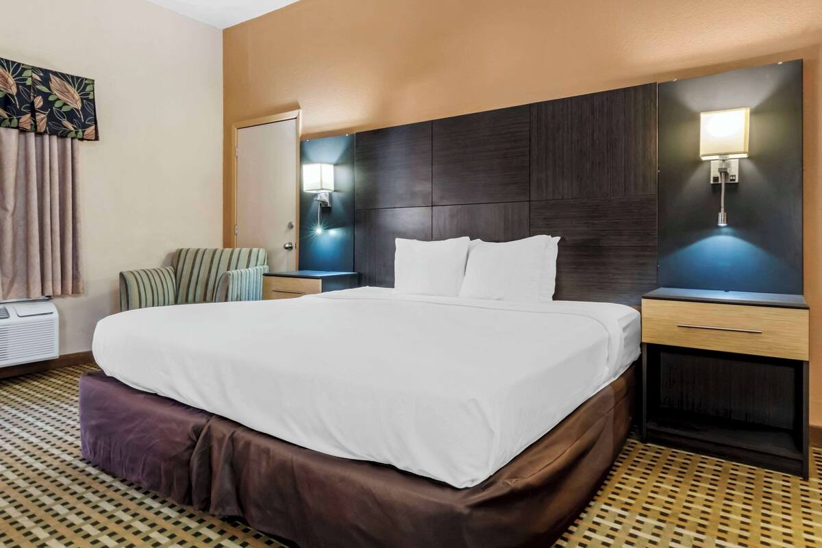 Habitación de hotel con una cama grande, una mesita de noche, una lámpara de pared y un suelo estampado.