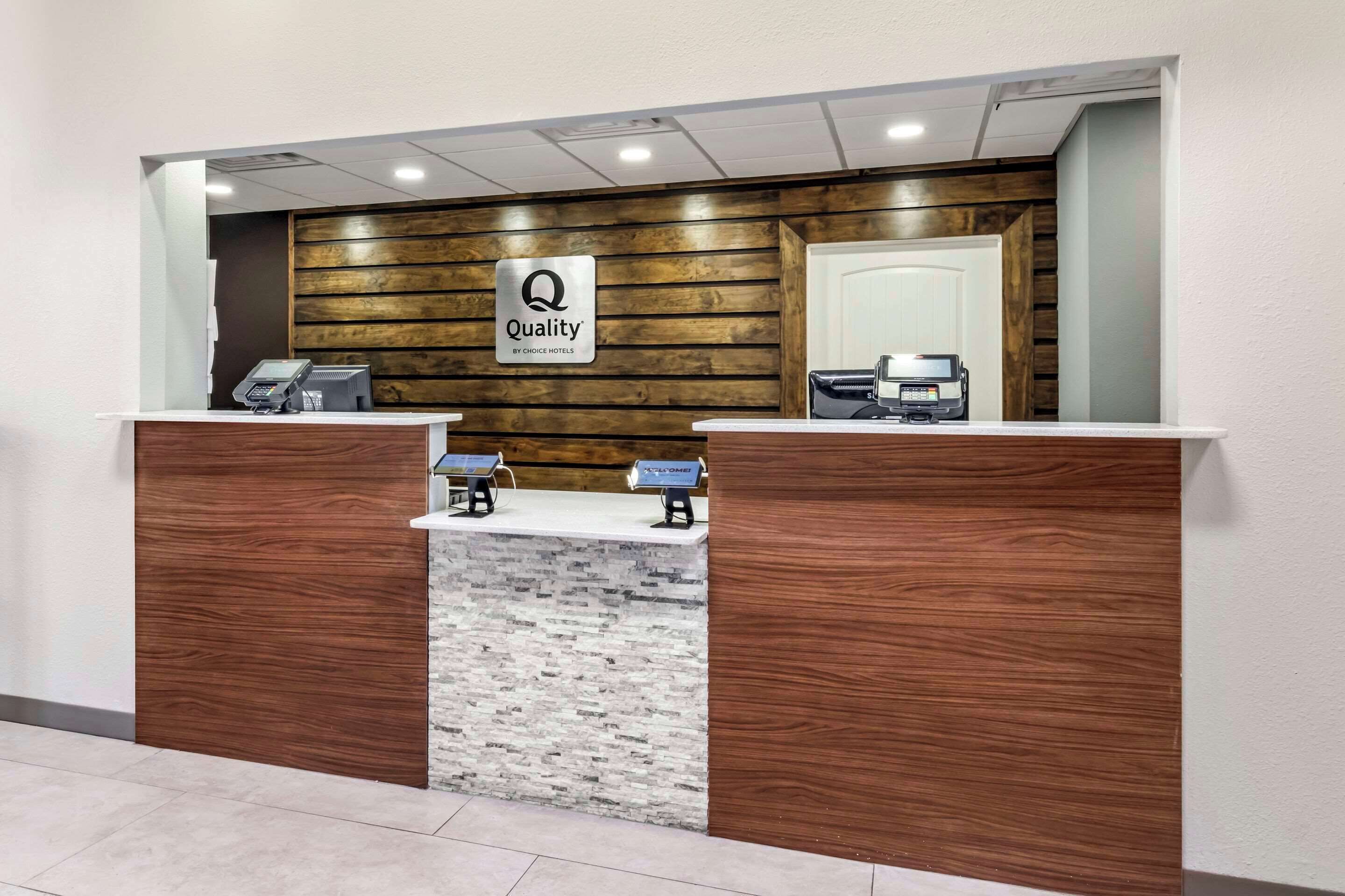 A reception desk with a wooden panel wall, a marble counter, and a sign that reads "Quality by Choice Hotels."