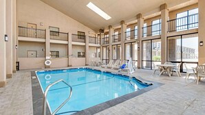 A large indoor swimming pool with multiple levels of balconies, clear glass walls, and a tiled floor.