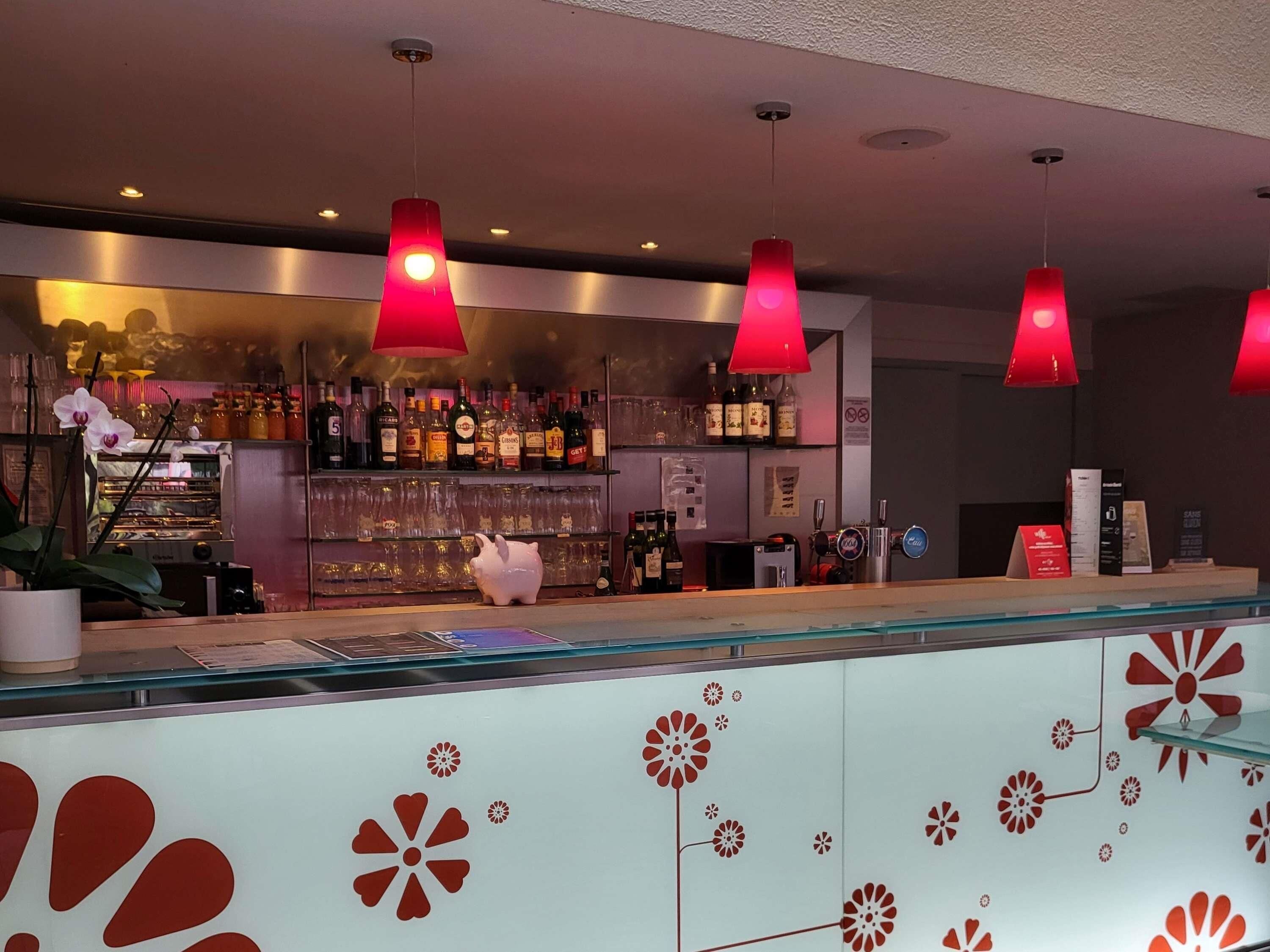 A bar area with red pendant lights, a glass display case, and a variety of bottles and glasses.