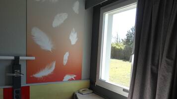 Una habitación con escritorio, teléfono, ventana con cortinas y un papel tapiz con diseño de plumas.