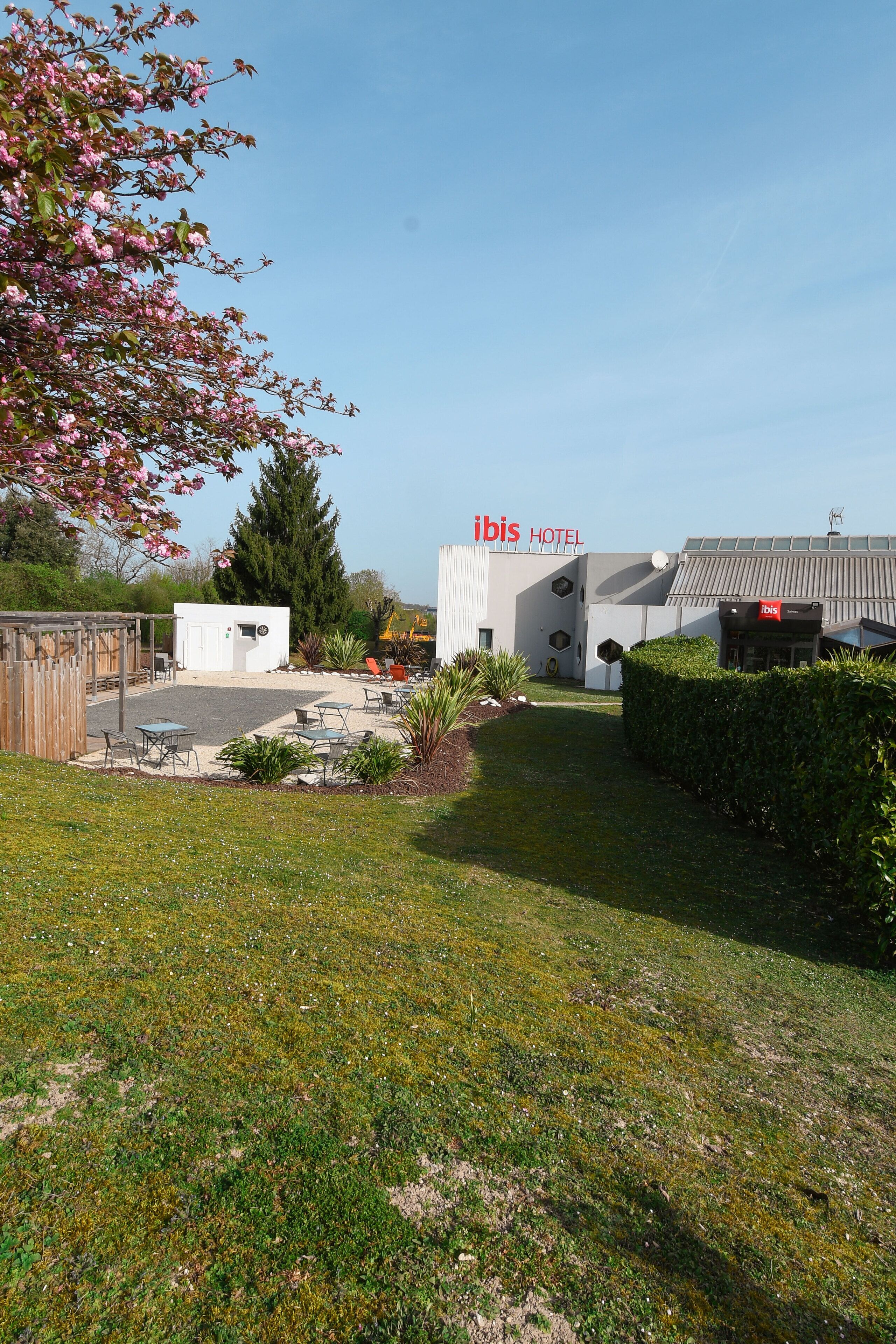 Un hotel Ibis con un patio, mobiliario exterior y un jardín bien cuidado.
