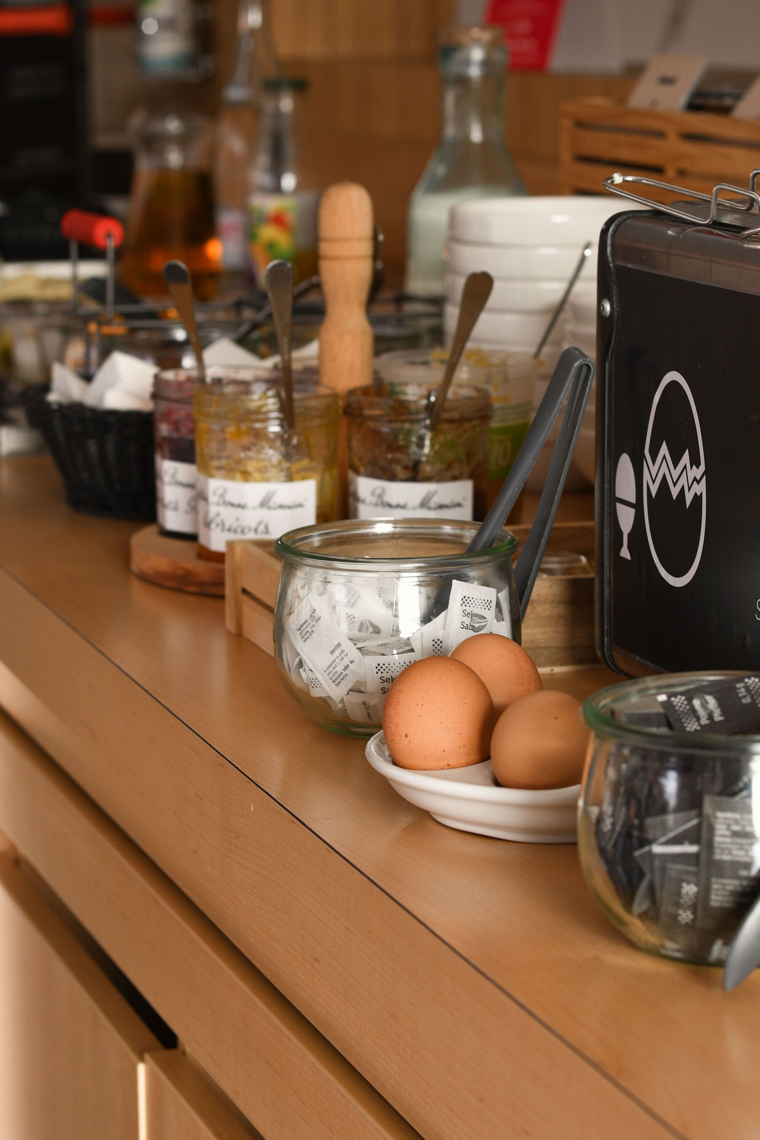 Una encimera de cocina con frascos diversos, una cuchara de madera y huevos.