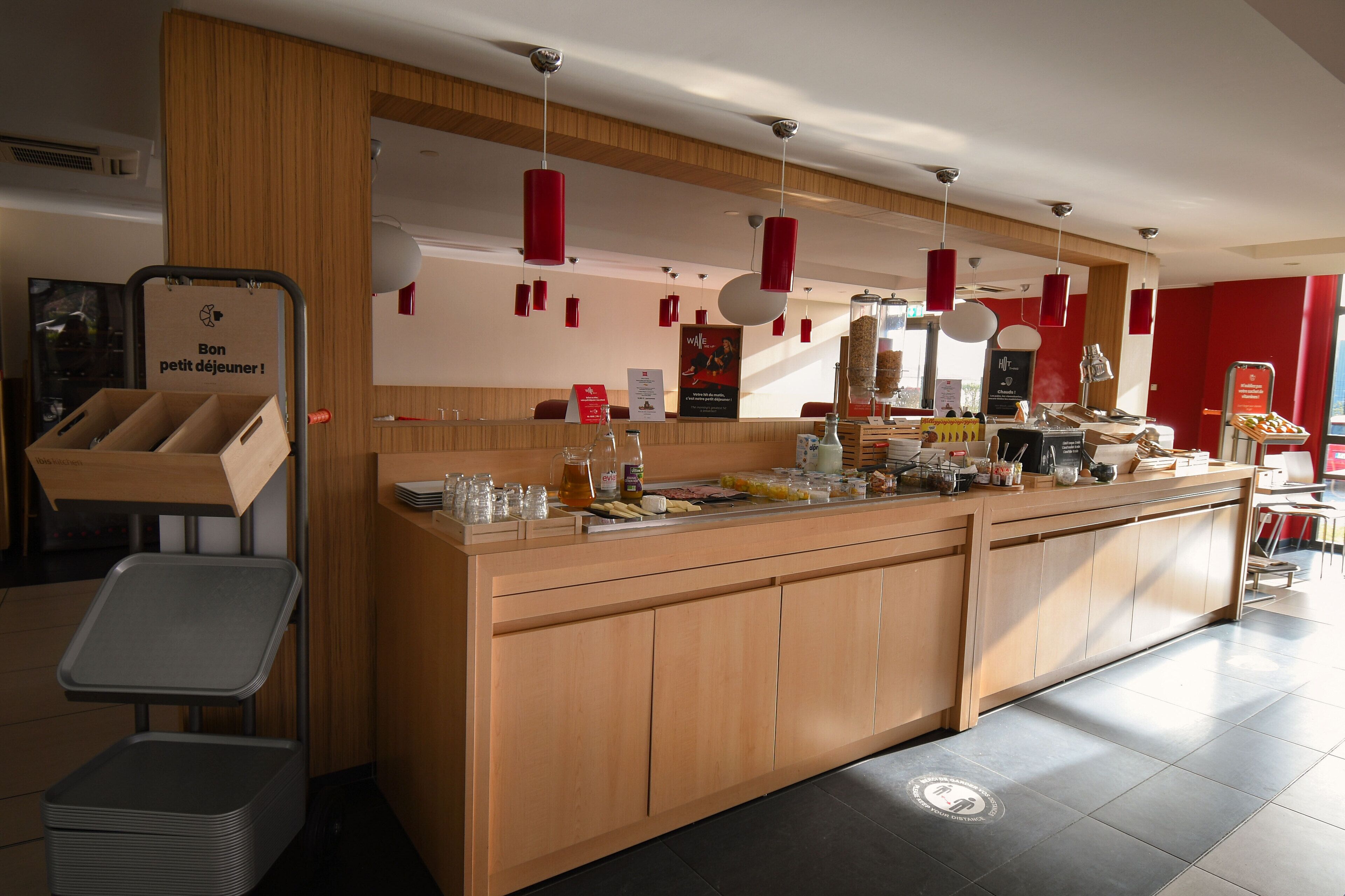 A modern café with a wooden counter, hanging red pendant lights, and a variety of food and drink items displayed.