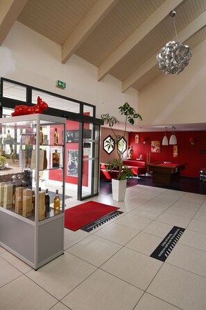 A lobby with a glass display case, red walls, a pool table, and a potted plant. - Hôtel ibis Saintes (Saintes)