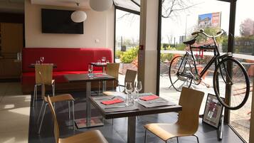 A modern dining area with a red couch, a table set for two, and a bicycle outside the window.