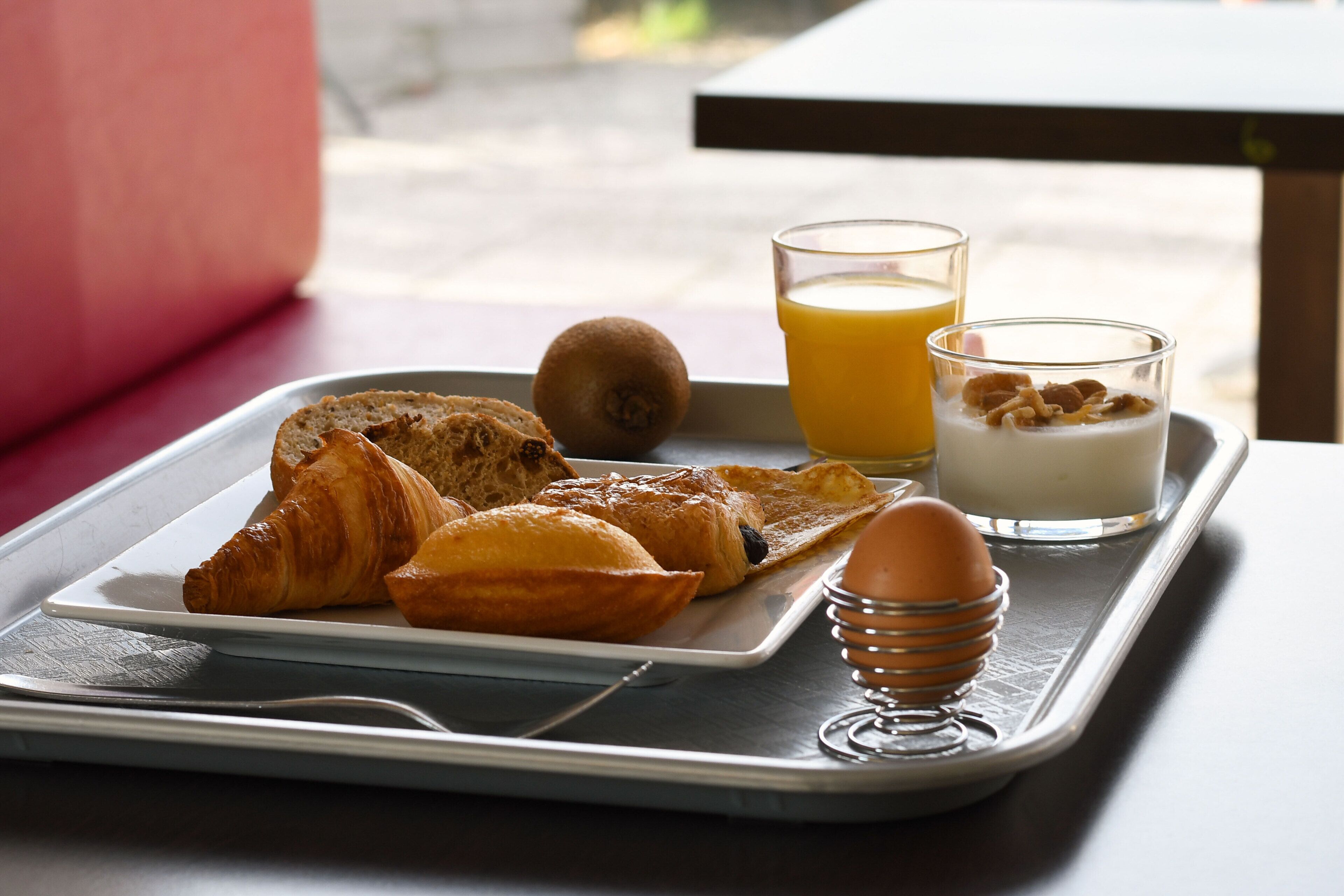 Un plateau de petit-déjeuner avec des croissants, un kiwi, un verre de jus d’orange, un verre de lait avec des céréales et un œuf dur, le tout posé sur une table.