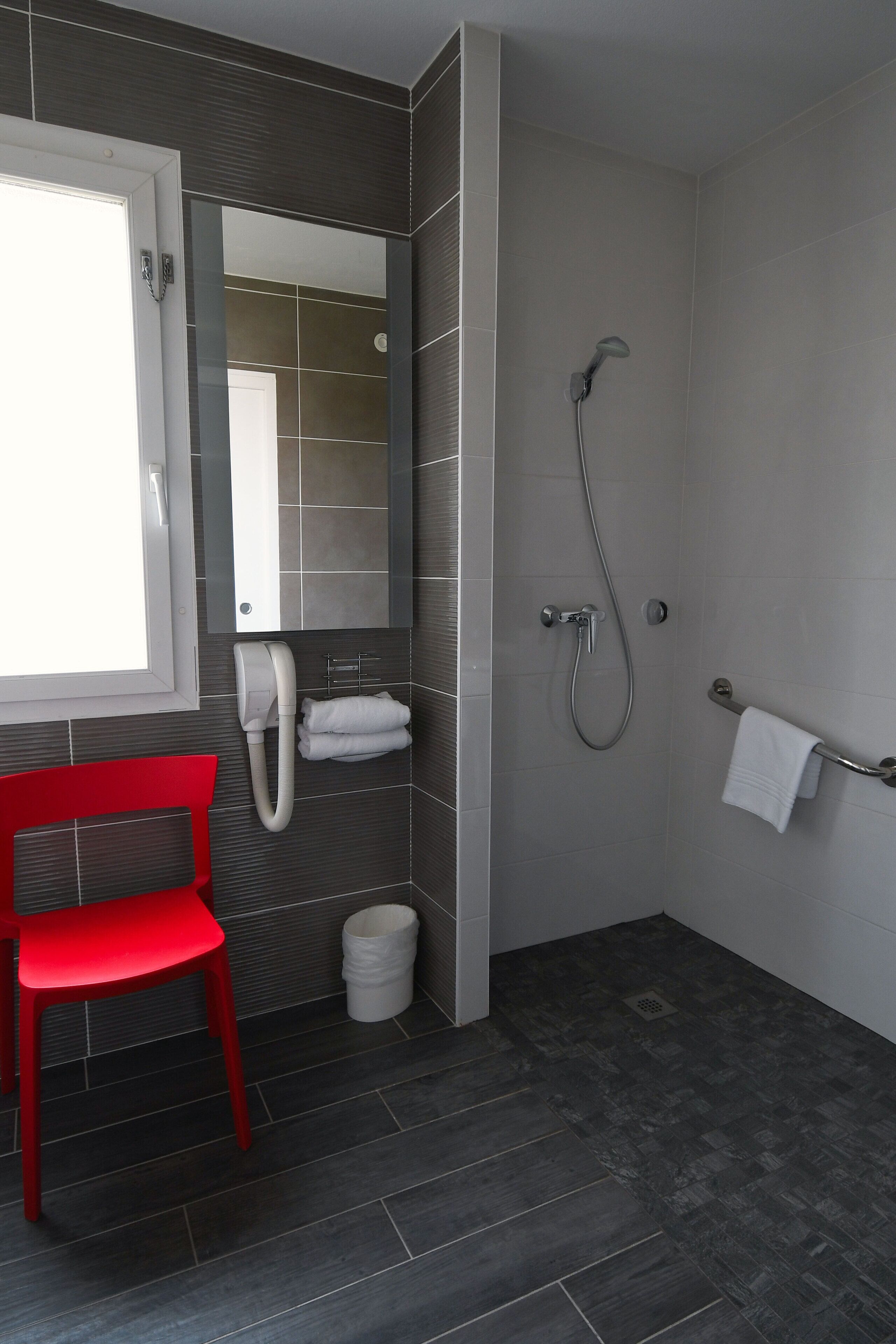 A modern bathroom with a shower, a red chair, and a towel rack.