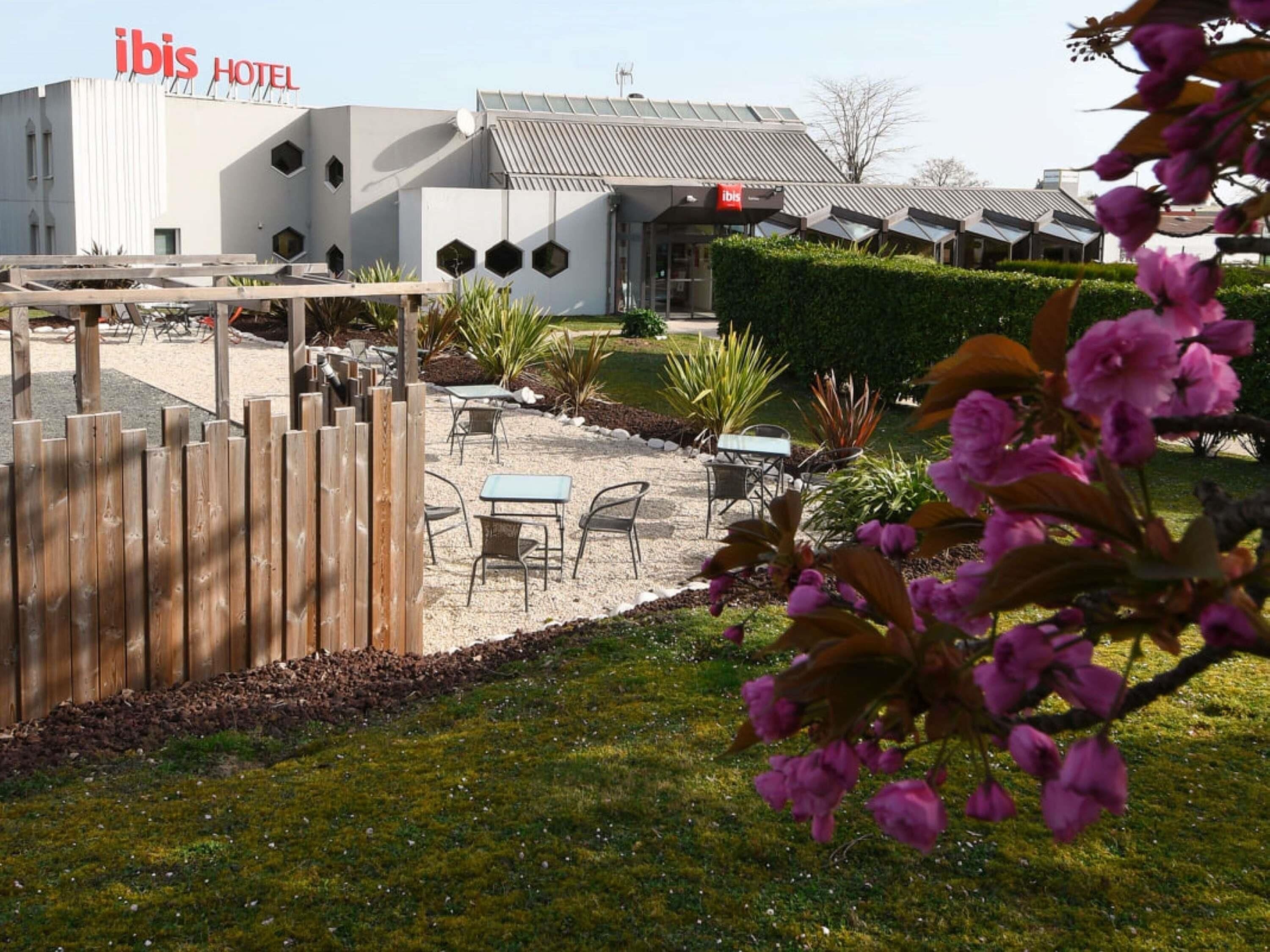 An ibis hotel with a modern architectural design, outdoor seating area, and a well-maintained garden.