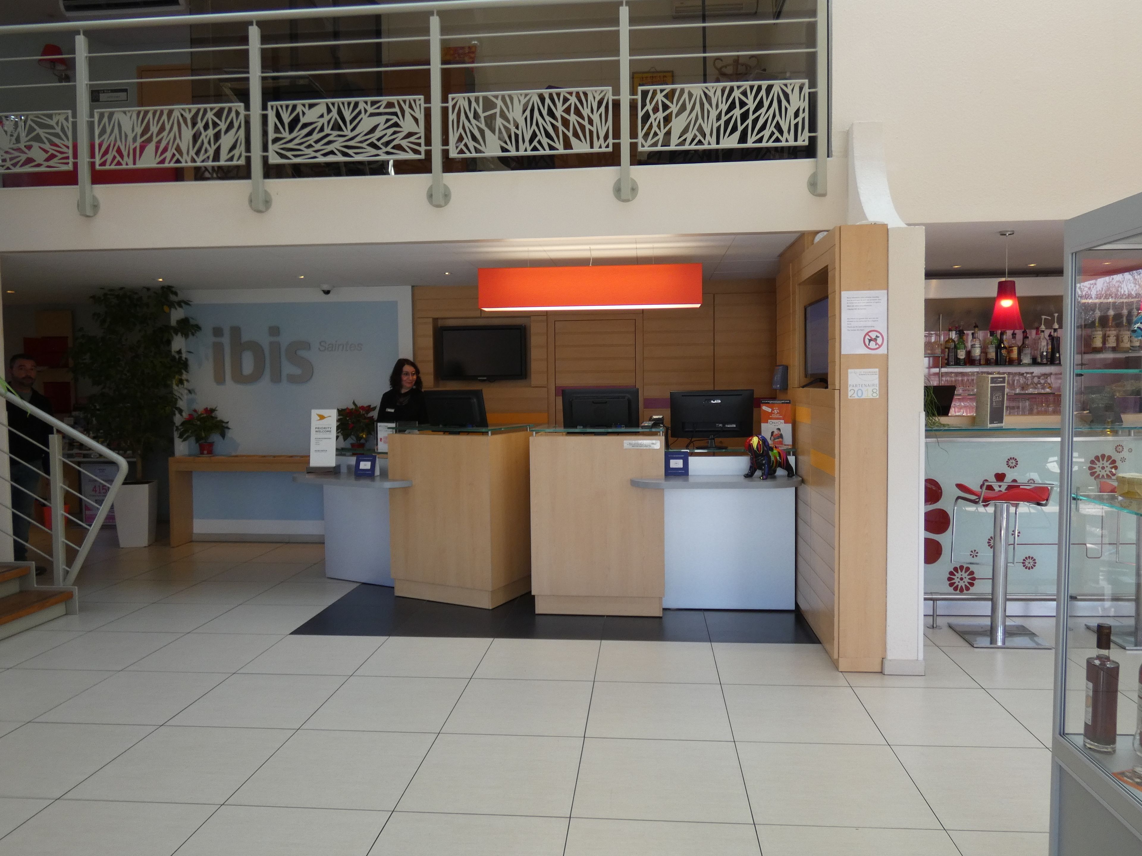 A reception area with a counter, a TV, and a sign that reads "ibis Saintes".