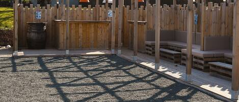 A wooden outdoor seating area with benches and tables, surrounded by a wooden fence.