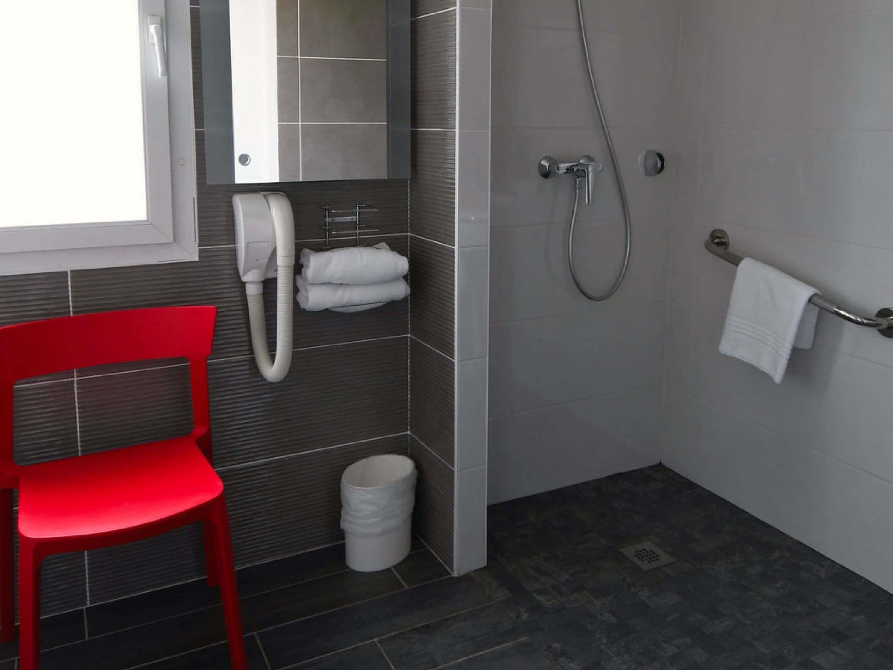 A modern bathroom with a red chair, a towel rack, a toilet, and a shower area.
